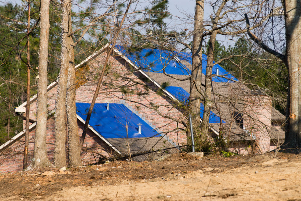 tornado damaged house with a blue tarpaulin on the roof