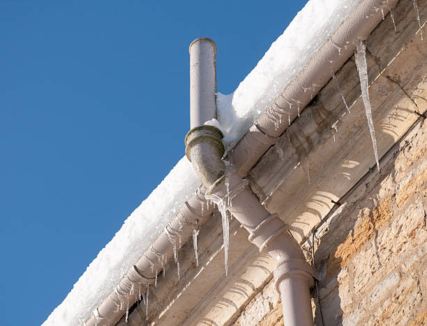 Icicles hanging from the gutter, and snow on the roof causing drainage problems for an old building in winter.